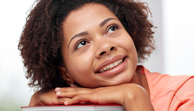 female student smiling while thinking with her head rested on books