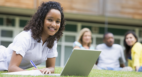 A girl using a lap top and completing math problems on a school lawn