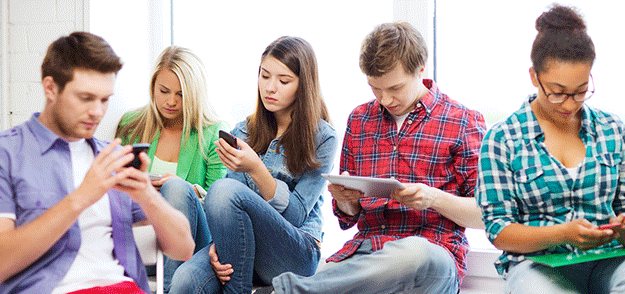 five students sitting and looking at cell phones and tablets