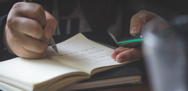 A student holdign a cellphone and writing in a notebook