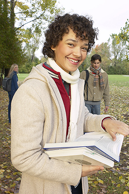 a teenager smiling and holding two books while outside on a fall day