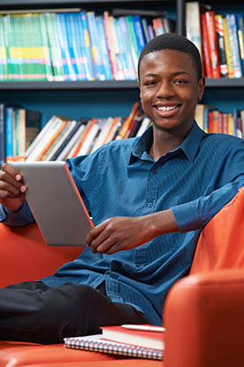 male student using a tablet in the library and sitting on a couch