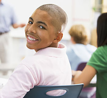 male student sitting at his desk and smiling