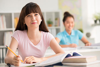 female teen studying in a classroom with fuzzy picture of a classmate in the background