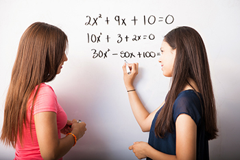 Two girls solving an equation on a white board