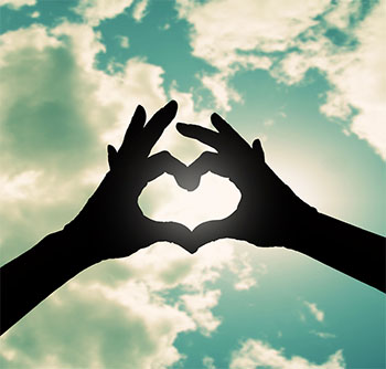 Hands making a heart with clouds behind