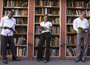 three students reading in front of bookshelves