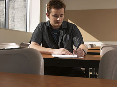 male student writing at a table