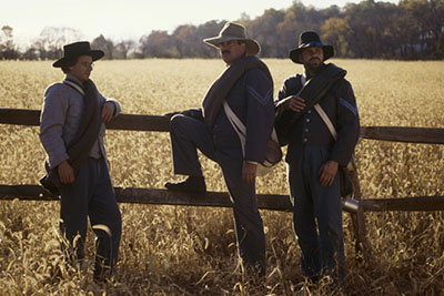 Civil War soldiers leaning on a wooden fence beside a wheat field