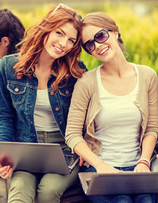 two smiling friends sitting with laptops