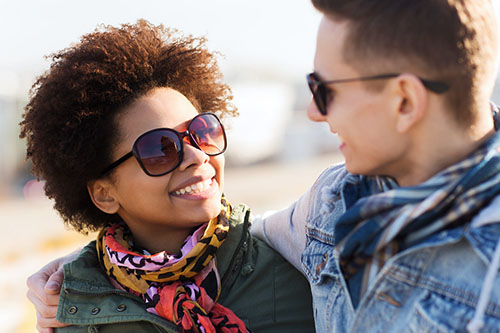 male and female facing each other, wearing sunglasses, and smiling