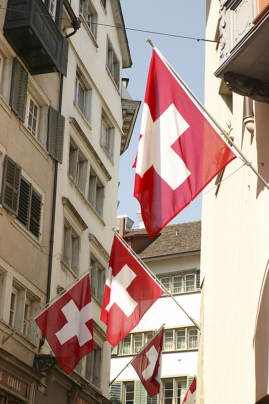 three flags of Switzerland hanging outside of apartment buildings