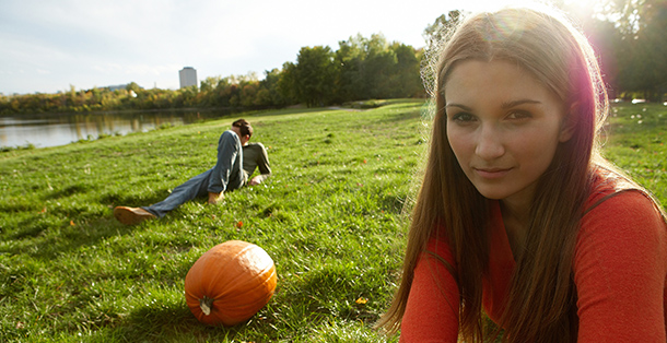 Girl and boy sitting in grass with a pumpkin between them