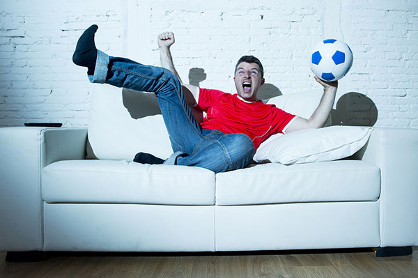 man on couch with arms raised holding a soccer ball