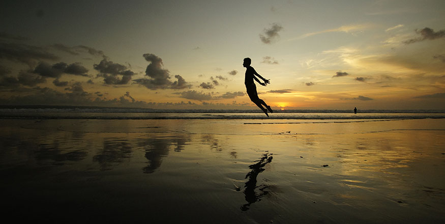 person jumping on the beach with reflection showing in the wet sand