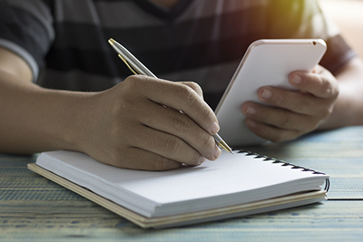 A student working on a mobile phone writing in a notebook