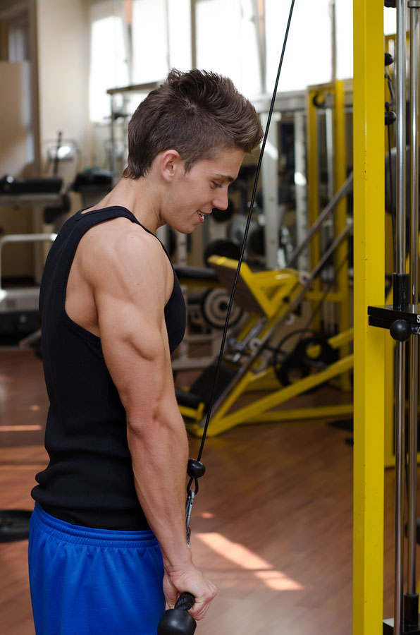 male teen working on on gym equipment with triceps cables