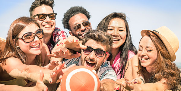 happy multcultural friends reaching for a football on the beach