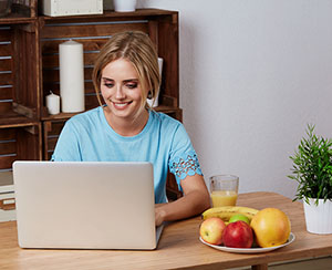 female on a computer with fruit in front of her