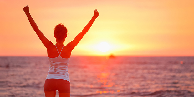 Girl at beach with sunset raising arms in celebration