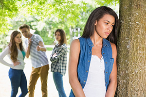 Teenager looking sad with peers behind her pointing