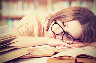 girl with glasses asleep with head on books