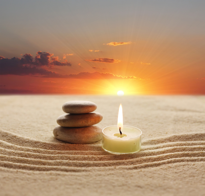 meditative stones and a candle resting in the sand with a sunset in the background