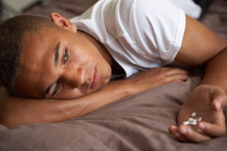 depressed male laying on bed with pills in hand