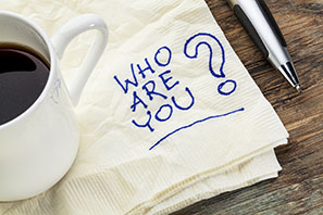 paper napkin with words written in blue ink that say "who are you." coffee mug on corner of napkin.