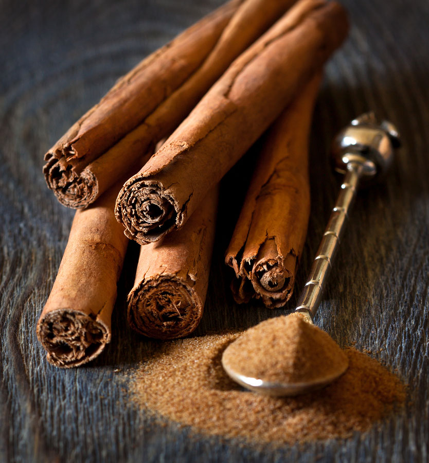 cinnamon sticks next to a silver spoon filled with granulated cinnamon