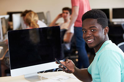 Student at the computer with cell phone in his hand