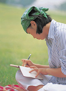 female sitting cross-legged on the ground outside, and writing in a journal