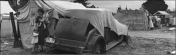 Image of mother and two children in front of an old car. 